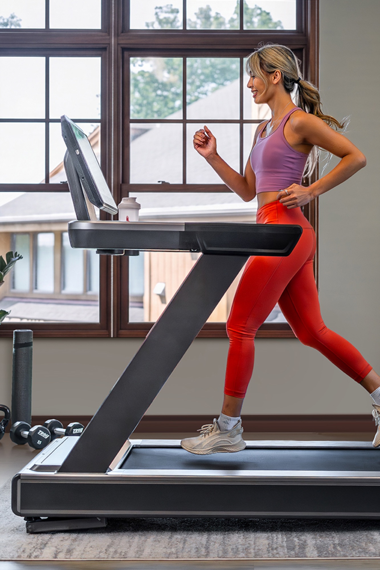 A woman in a purple tank top and red leggings jogging on a treadmill.